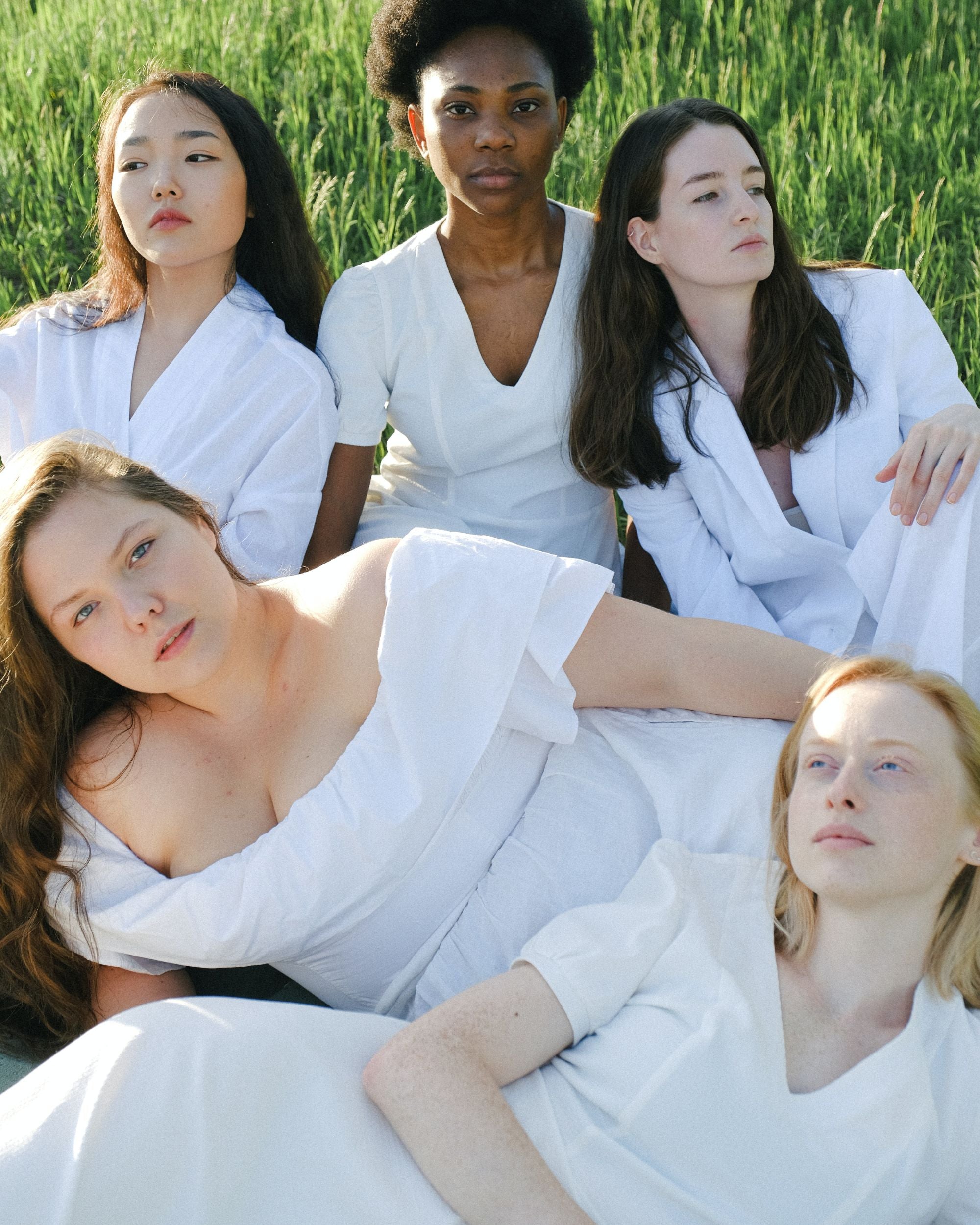 Diverse Women in white clothing sitting on green grass in a field