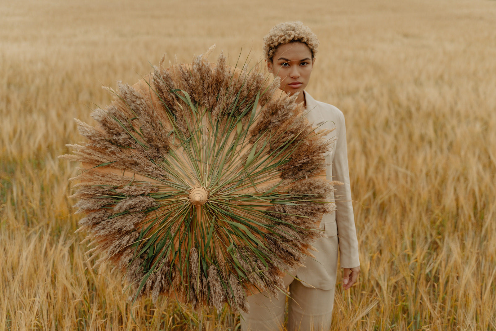 Women in cream pant suit and short hair with umbrella standing in a field of grass
